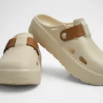 Vista frontal de par de zuecos de plataforma Concept Shoes en color hueso con correa lisa de color café sobre fondo blanco.