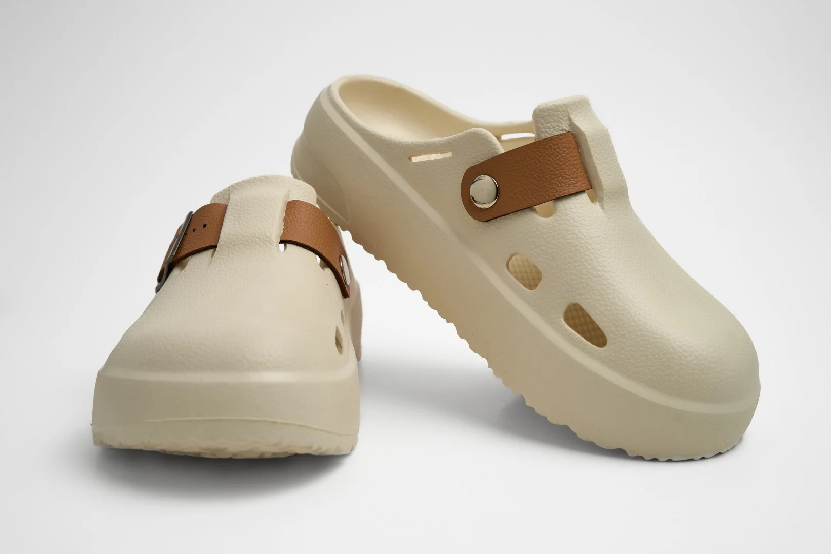 Vista frontal de par de zuecos de plataforma Concept Shoes en color hueso con correa lisa de color café sobre fondo blanco.