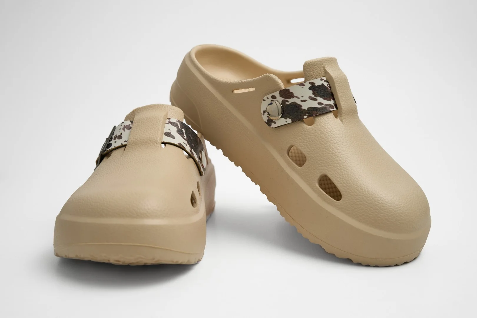 Vista frontal de par de zuecos de plataforma Concept Shoes en color beige topo con empeine liso y correa de estampado cowprint sobre fondo blanco.