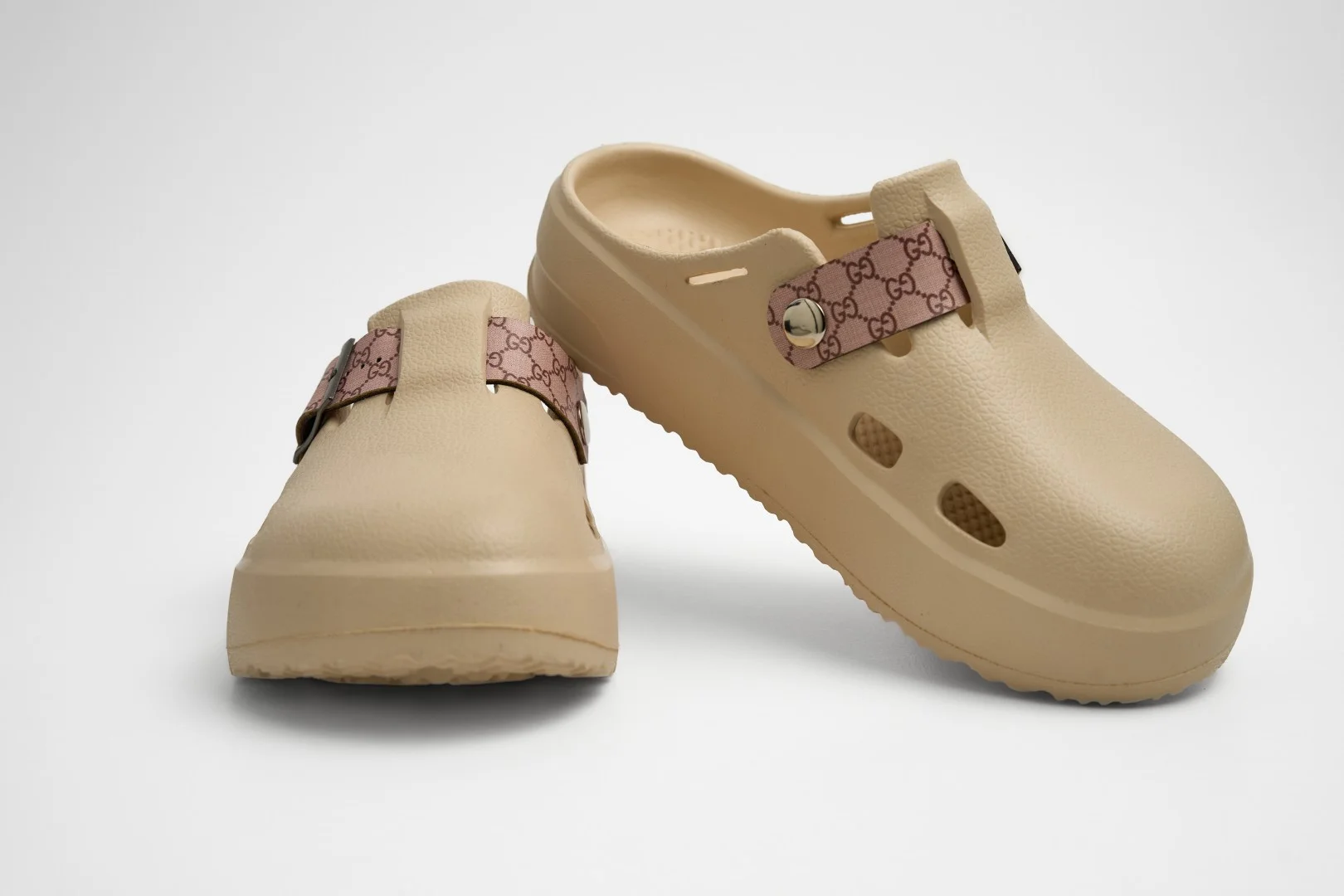 Vista frontal de par de zuecos de plataforma Concept Shoes en color beige con empeine liso y correa de patrón monograma rosa sobre fondo blanco.