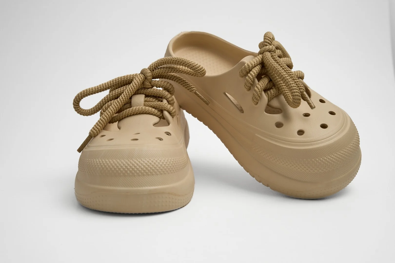 Vista frontal de par de zuecos de plataforma Concept Shoes en color beige topo texturizados con audaces cordones de soga sobre fondo blanco.