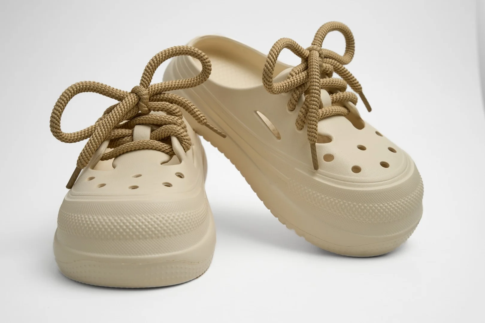 Vista frontal de par de zuecos de plataforma Concept Shoes en color hueso granulados con audaces cordones de soga café sobre fondo blanco.