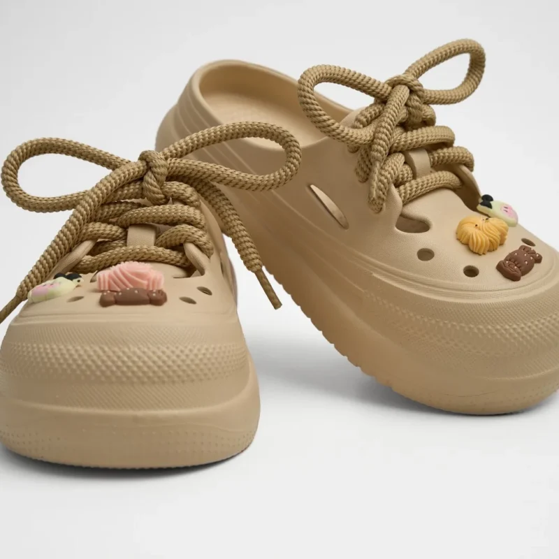 Vista frontal de un par de zuecos de plataforma EVA Concept Shoes color beige neutro con cordones de soga y pines tiernos sobre fondo blanco.