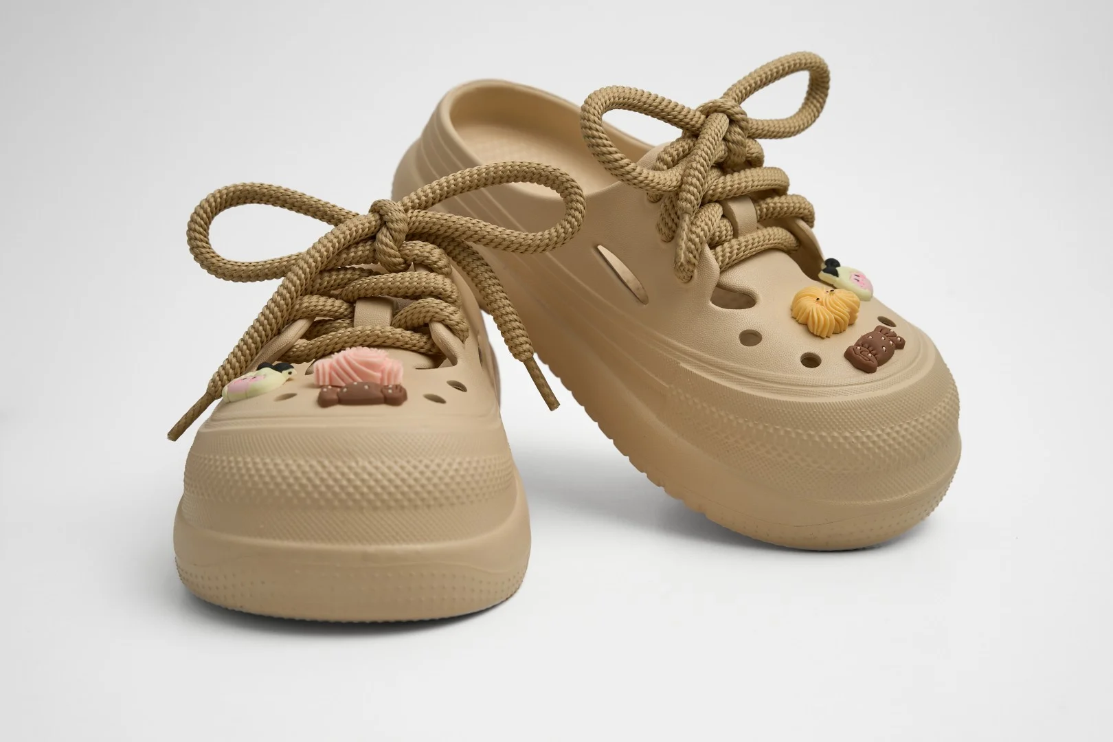 Vista frontal de un par de zuecos de plataforma EVA Concept Shoes color beige neutro con cordones de soga y pines tiernos sobre fondo blanco.